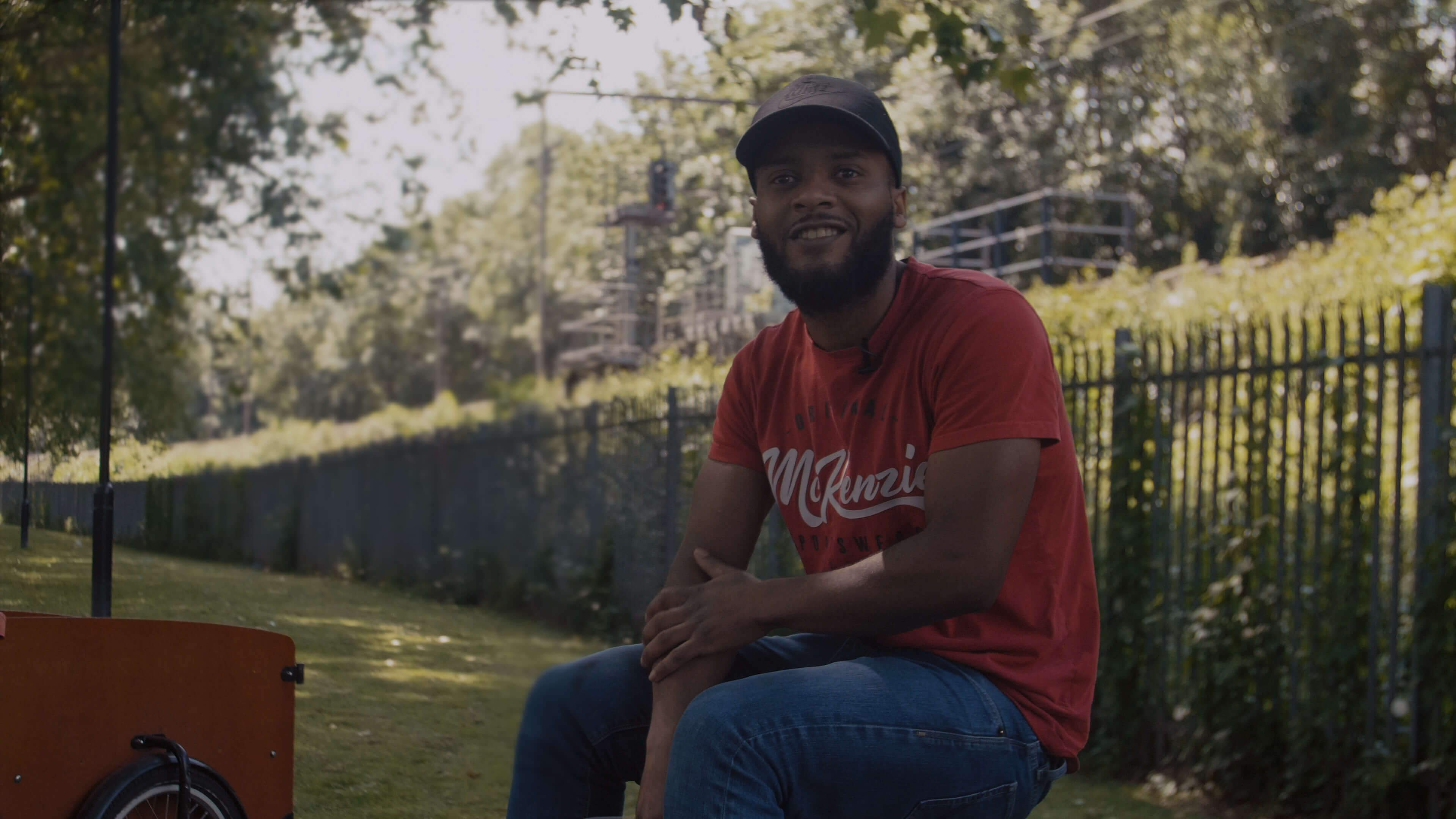 A man smiling while surrounded by trees and giving interview to camera